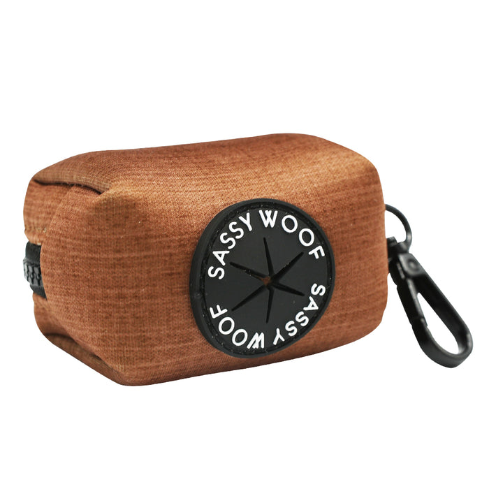 The Sassy Woof Dog Four Piece Bundle - Teddy includes a brown fabric waste bag holder with a black plastic clip, circular logo, and star-shaped bag dispenser—perfect for walks with your adjustable harness.