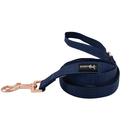 A rolled-up navy blue dog leash from the Sassy Woof Dog Four Piece Bundle - Twilight, featuring a rose gold clip and black label, displayed on white. Ideal to pair with an adjustable harness for your puppy's growth plan.