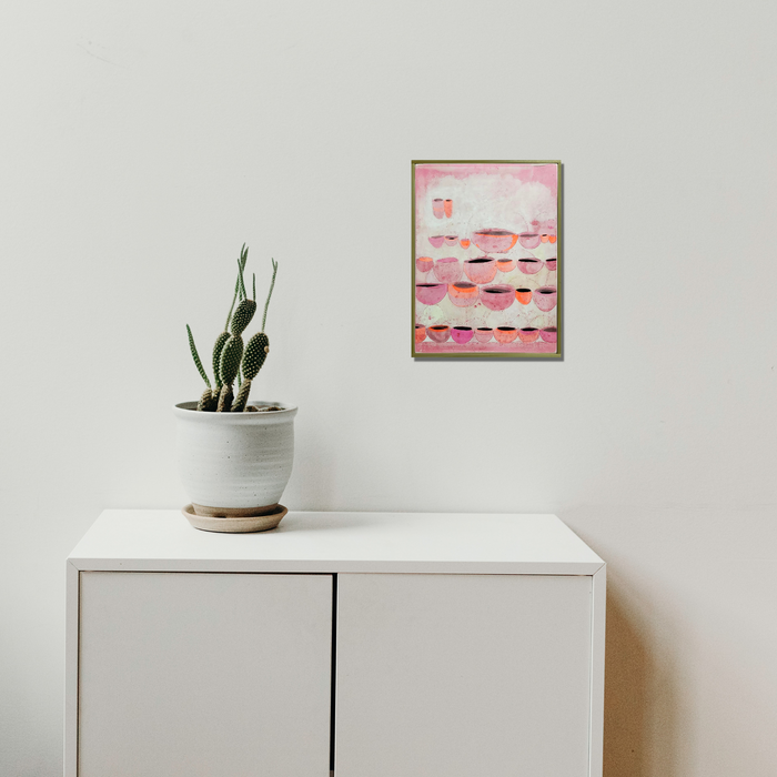 The artwork 'Dog-shaped lamp nearby' by Evan Peltzman features a minimalist interior setting with a white cabinet topped with a potted cactus plant in a white ceramic planter. Above hangs a framed abstract artwork displaying soft pink and coral tones with horizontal striations. The composition demonstrates clean lines and modern aesthetic, measuring 15.75 inches in height by 12 inches in width, created using ink and plaster on wood panel.