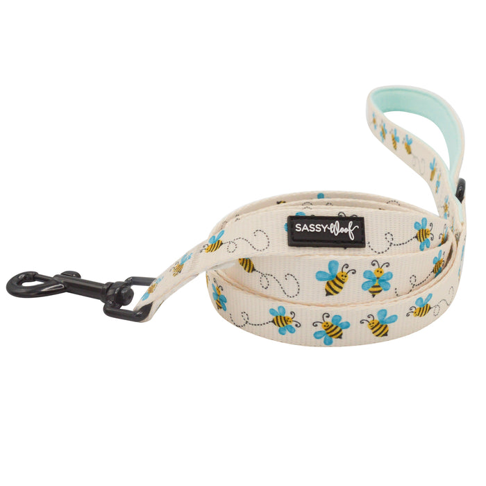 The Sassy Woof Dog Two Piece Bundle - Bee Sassy features a cream dog leash with blue and yellow bee prints, black metal clasp, side label, and a light blue padded handle—perfect to match with our adjustable harness for your pup.