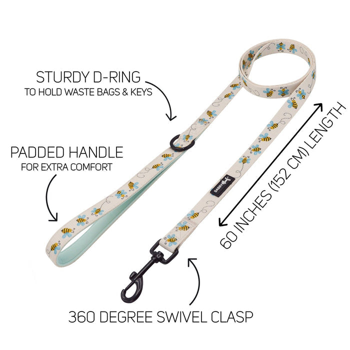 The Sassy Woof Dog Two Piece Bundle - Bee Sassy includes a cream-colored leash with bee pattern, padded handle, sturdy D-ring, 360° swivel clasp (60"/152 cm), and an adjustable harness for extra comfort—features labeled by arrows.