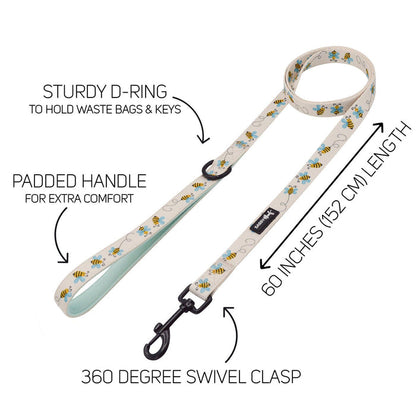 The Sassy Woof Dog Two Piece Bundle - Bee Sassy includes a cream-colored leash with bee pattern, padded handle, sturdy D-ring, 360° swivel clasp (60"/152 cm), and an adjustable harness for extra comfort—features labeled by arrows.