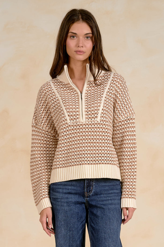 Woman wearing a beige knitted sweater with a white zipper against a beige background