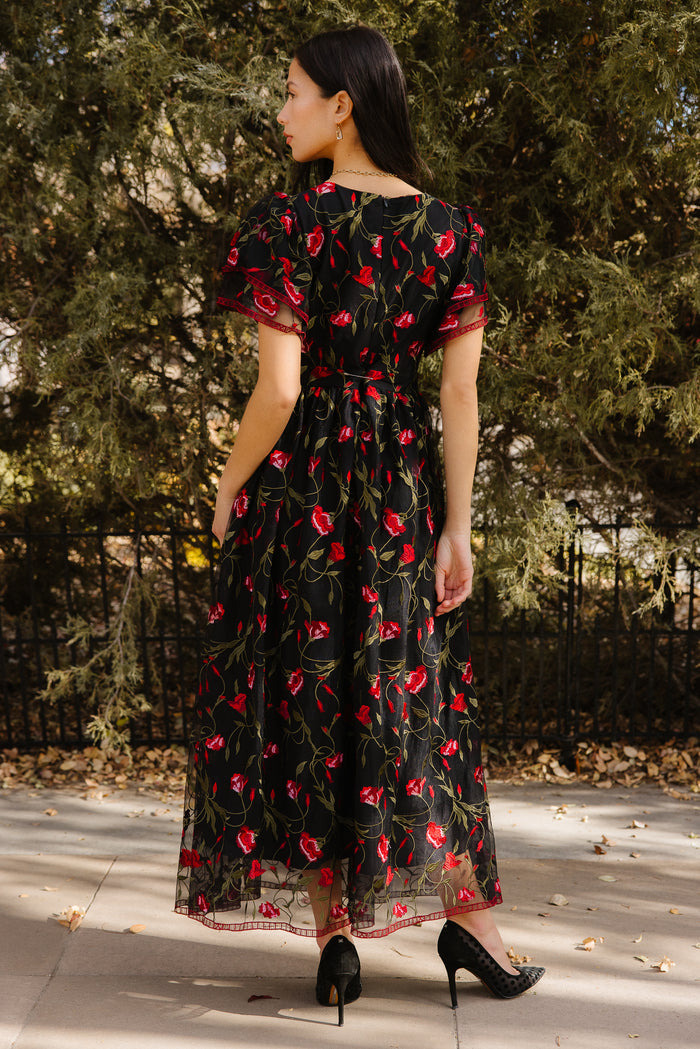 Woman wearing a black floral dress standing outdoors with trees in the background