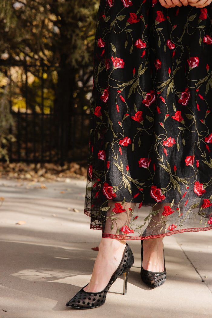 Bottom half of a black floral dress outside in front of trees