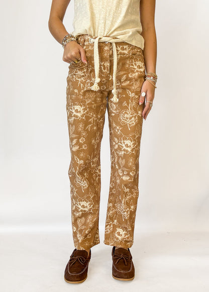 A person wearing tan pants with a cream floral print and a cream drawstring waist
