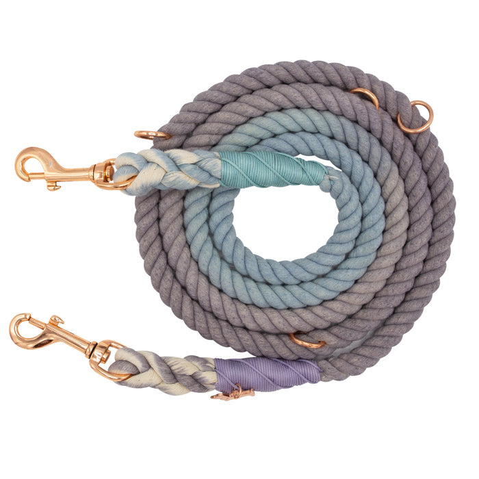 Introducing the Sassy Woof Hands-Free Rope Leash - Skyfall: an adjustable coiled rope dog leash showcasing a striking ombré gradient from grey to blue. Designed with rose gold metal clasps at both ends and intricate woven accents near the clasps, this leash seamlessly blends style and functionality for your daily walks.