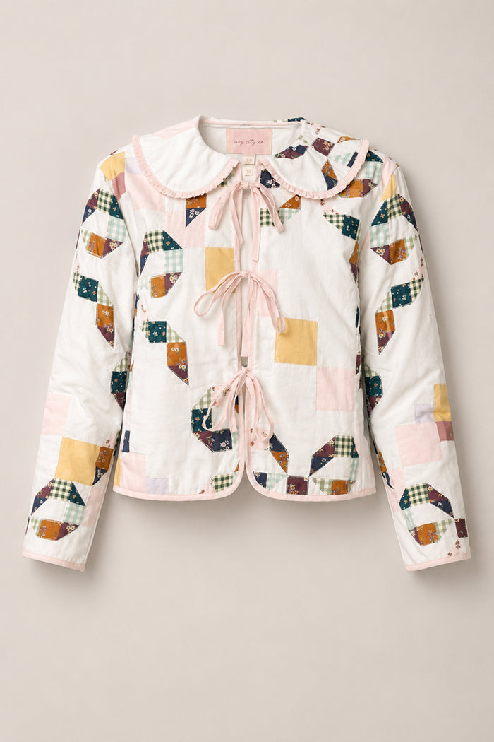 The Harper Jacket in Quilted Bow by Ivy City Co is a charming women’s jacket crafted from soft cotton, featuring pastel and plaid patchwork quilting, a scalloped collar, and pink ribbon ties on the front. Displayed on a beige background, this stylish piece offers both comfort and elegance.