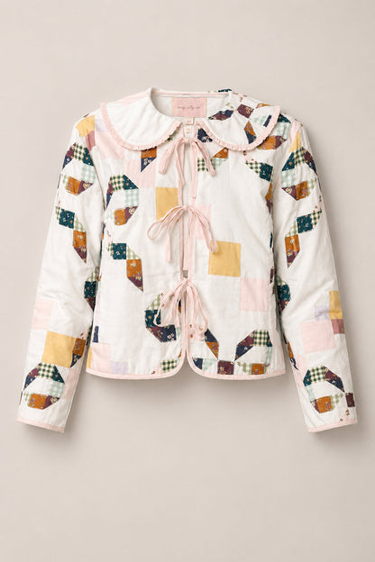 The Harper Jacket in Quilted Bow by Ivy City Co is a charming women’s jacket crafted from soft cotton, featuring pastel and plaid patchwork quilting, a scalloped collar, and pink ribbon ties on the front. Displayed on a beige background, this stylish piece offers both comfort and elegance.