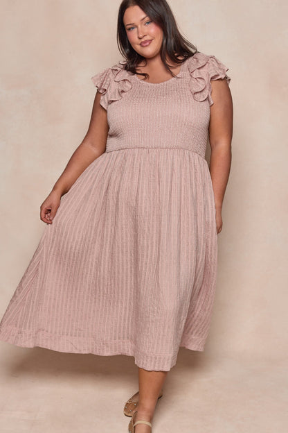 A woman smiles as she stands against a neutral background, holding one side of her Ivy City Co Hattie Dress in Pink Stripes—a sleeveless midi with smocked bodice and ruffled shoulders—paired with strappy sandals.