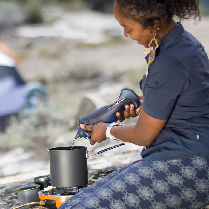 Lifestyle image of a woman squeezing water form a LifeStraw 1000ml filter bottle in to a camp cooking pot