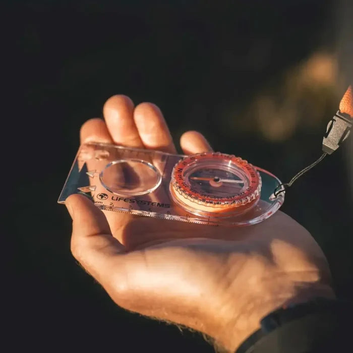 Hand holding a Lifesystems Hiking Compass with a blurred natural background