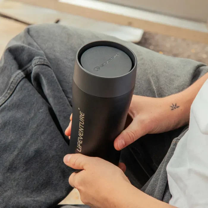 Person holding a Lifeventure One Touch Stainless Steel Thermal Mugs 350ml black in their lap whilst seated outdoors.