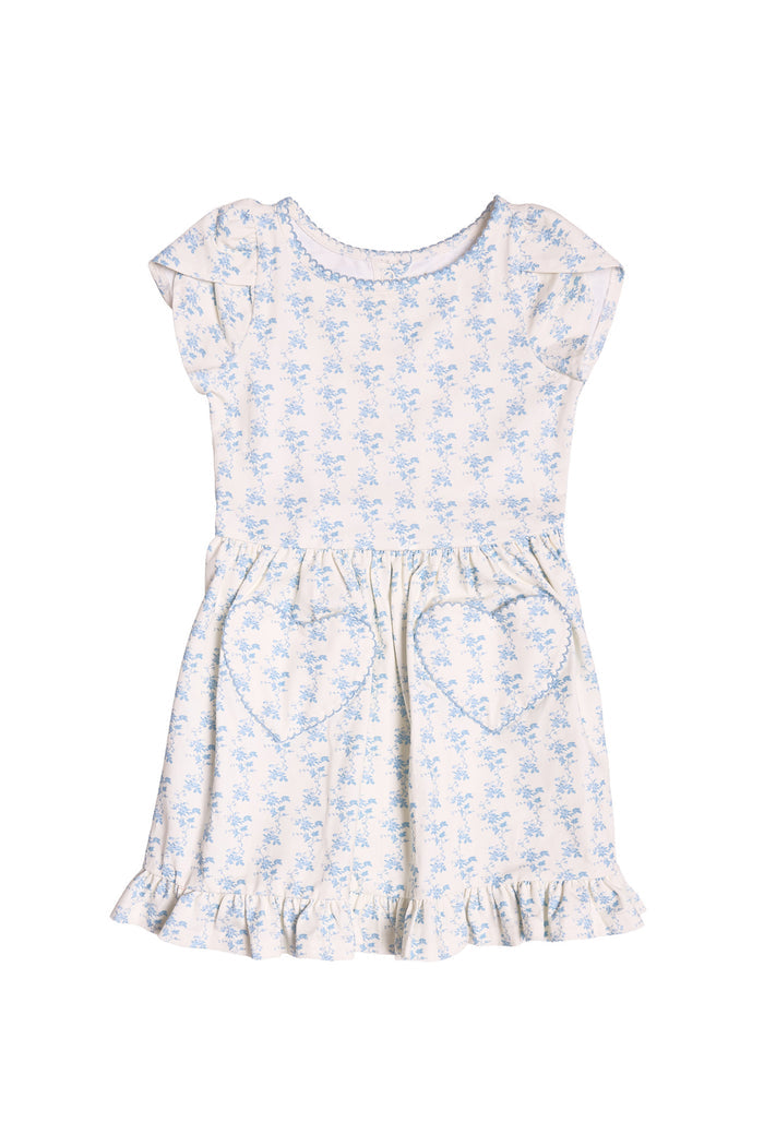 The Mini Dream Play Dress in Ivory Porcelain Fleur by Ivy City Co is a short-sleeved girls’ cotton dress with blue floral prints, heart front pockets, and a ruffled hem—perfect for playtime and shown on a white background.
