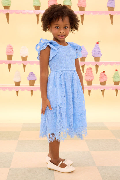 Young girl in a blue dress standing in front of an ice cream cone display.