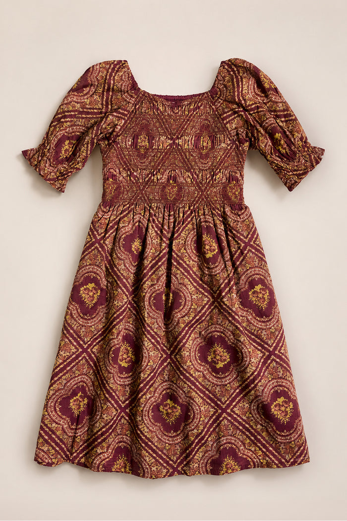 Mini Josephine Dress in Nocturne Diamond Rose by Ivy City Co, featuring gold and pink ornate geometric patterns, puff sleeves, a smocked bodice, and a knee-length gathered skirt, laid flat on a light background.