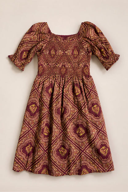 Mini Josephine Dress in Nocturne Diamond Rose by Ivy City Co, featuring gold and pink ornate geometric patterns, puff sleeves, a smocked bodice, and a knee-length gathered skirt, laid flat on a light background.