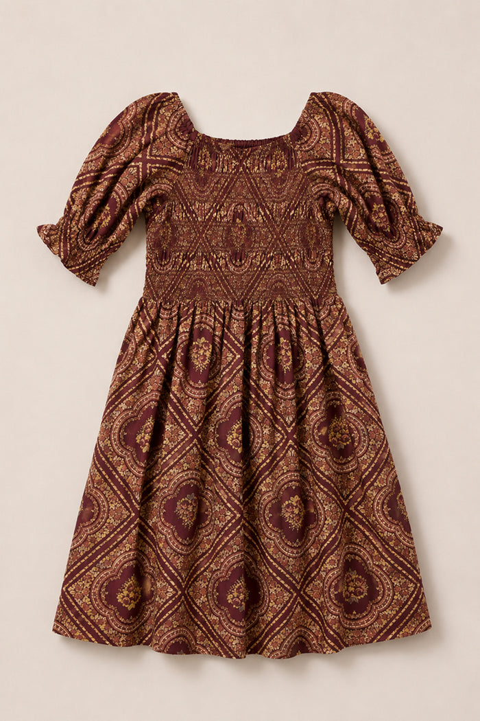 The Ivy City Co Mini Josephine Dress in Nocturne Diamond Rose showcases a brown and maroon diamond rose pattern with puff sleeves, a fitted smocked bodice, and a knee-length flared skirt, laid flat on a neutral background.