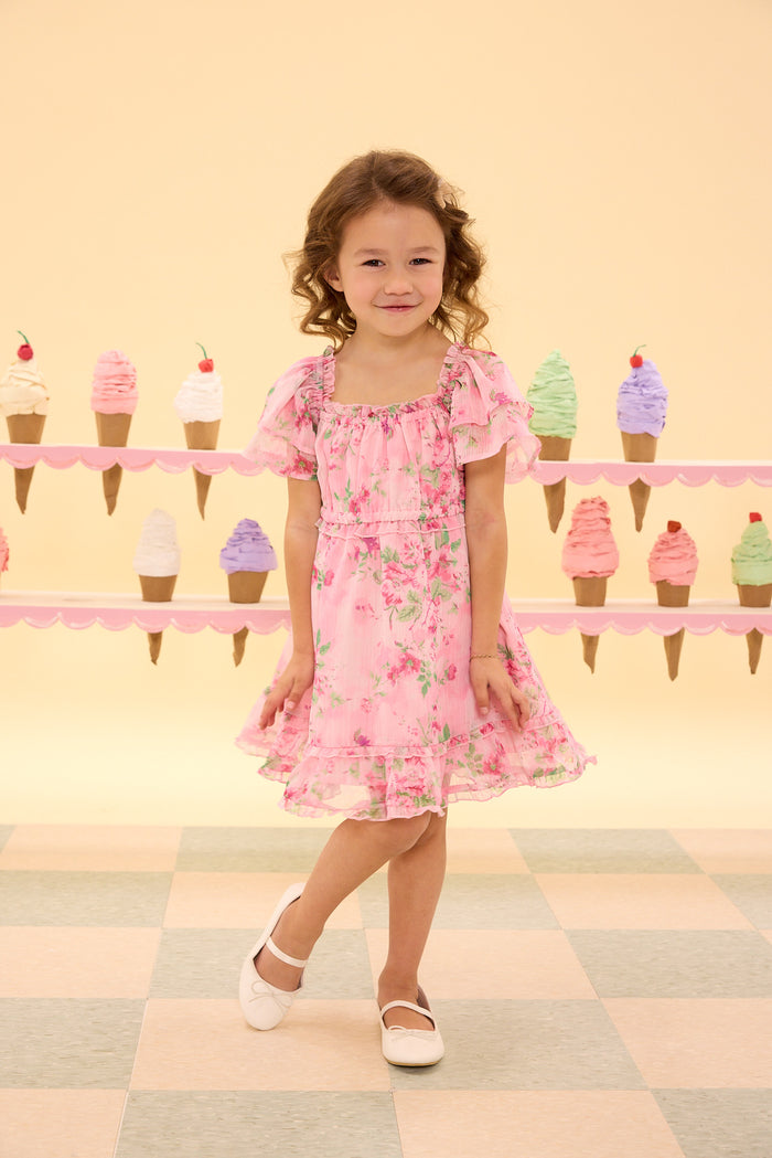Young girl in a pink floral dress standing in front of a colorful ice cream cone display.