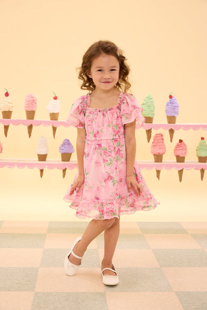 Young girl in a pink floral dress standing in front of a colorful ice cream cone display.