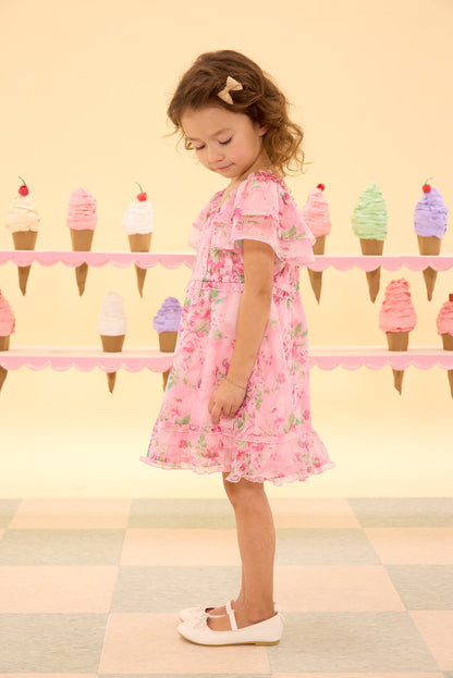 Young girl in a pink floral dress standing in front of ice cream cone decorations.