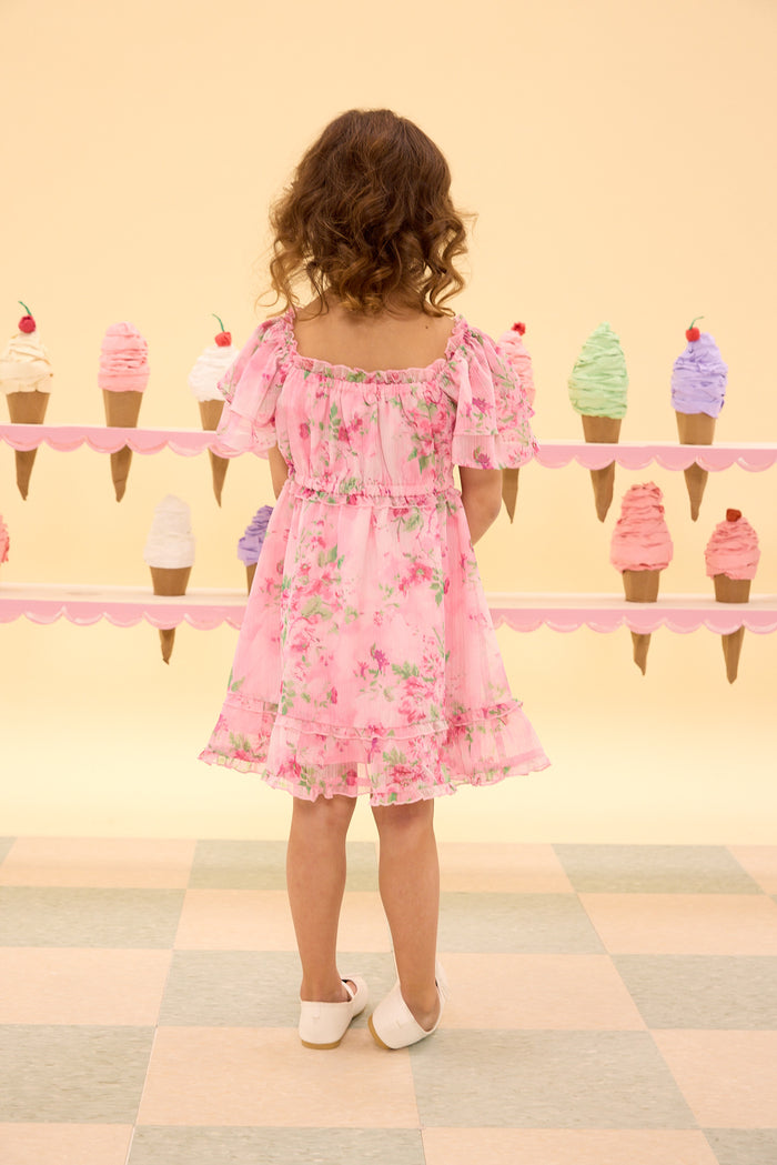 Child in a pink floral dress standing in front of ice cream cone decorations on a checkered floor.