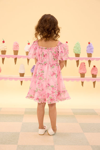 Child in a pink floral dress standing in front of ice cream cone decorations on a checkered floor.