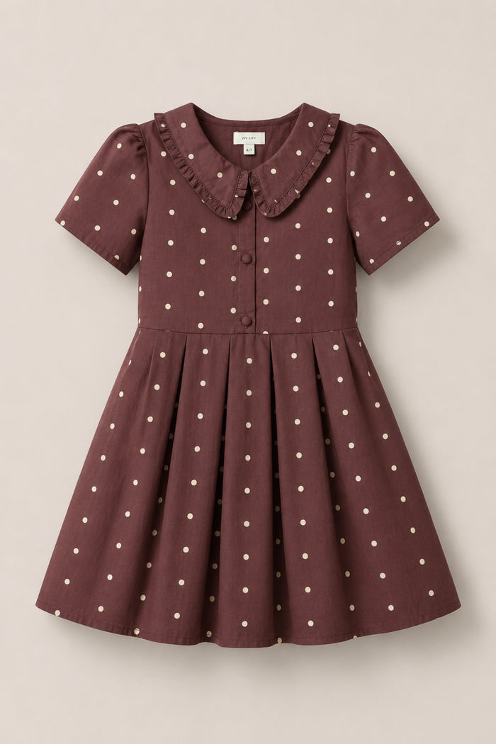 The Ivy City Co Mini Kit Dress in Warm Cocoa Dainty Dot features short sleeves, soft cotton fabric adorned with white polka dots, a ruffled Peter Pan collar, front buttons, and a pleated skirt. Displayed on a plain background, this dress offers both comfort and charm for any occasion.