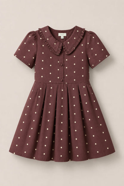 The Ivy City Co Mini Kit Dress in Warm Cocoa Dainty Dot features short sleeves, soft cotton fabric adorned with white polka dots, a ruffled Peter Pan collar, front buttons, and a pleated skirt. Displayed on a plain background, this dress offers both comfort and charm for any occasion.