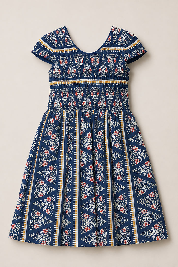 Introducing the Ivy City Co Mini Marlow Cap Sleeve Dress in Navy Fleur—a short-sleeved, knee-length cotton midi dress showcasing a charming blend of white, red, and yellow floral and striped patterns on a navy blue background. This dress features a fitted bodice and a flared skirt for an elegant silhouette.