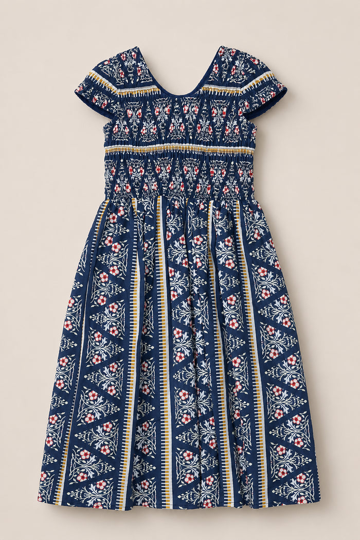 Introducing the Mini Marlow Cap Sleeve Dress in Navy Fleur by Ivy City Co—this charming navy blue cotton midi dress showcases short cap sleeves, a gathered bodice, and a pleated skirt. Adorned with white, red, and yellow floral and geometric striped patterns, it features a V-shaped back neckline for an effortlessly elegant look.