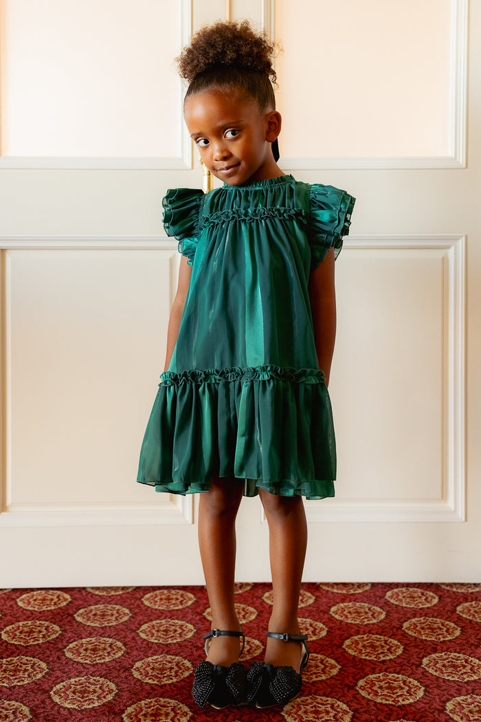 little girl in a green dress against a white wall