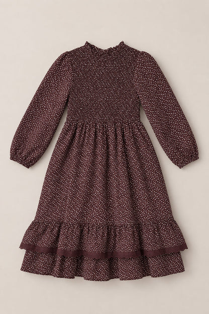 The Mini Presley Maxi Dress in Mahogany Ditsy by Ivy City Co features long balloon sleeves, a maroon background with tiny white polka dots, a smocked bodice, ruffled cuffs, and a tiered ruffle hem. The dress is shown laid flat on a neutral background.