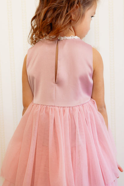 the back of a little girl in a pink dress standing against a white wall