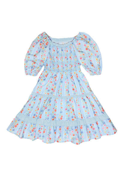 The Ivy City Co Mini Roselyn Dress in Blue Linear Floral Print features puff sleeves, a smocked bodice, a knee-length tiered skirt, and scattered red, yellow, and blue flowers for a charming look.