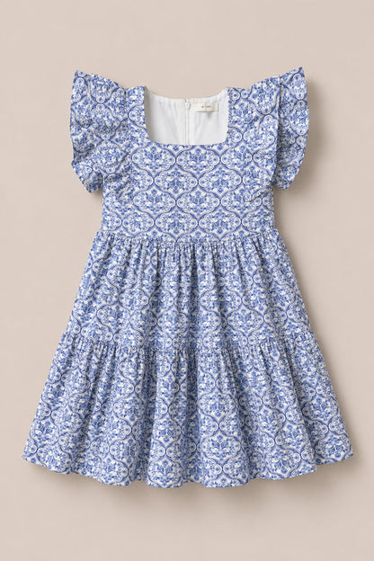 The Mini Trixie Dress in Blue Moroccan Tile by Ivy City Co is a girls' summer dress featuring a blue and white pattern, square neckline, ruffled sleeves, and a tiered skirt, inspired by Moroccan tile designs.