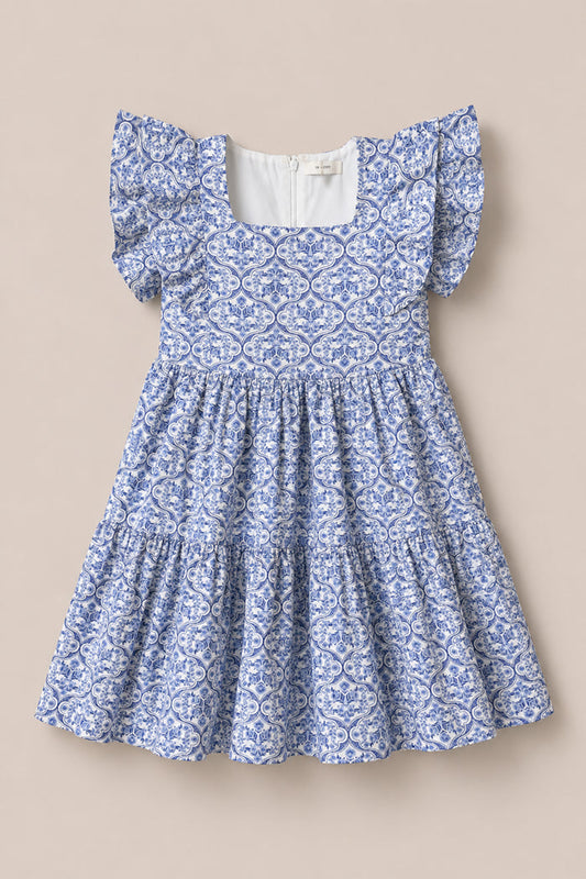 The Mini Trixie Dress in Blue Moroccan Tile by Ivy City Co is a girls' summer dress featuring a blue and white pattern, square neckline, ruffled sleeves, and a tiered skirt, inspired by Moroccan tile designs.