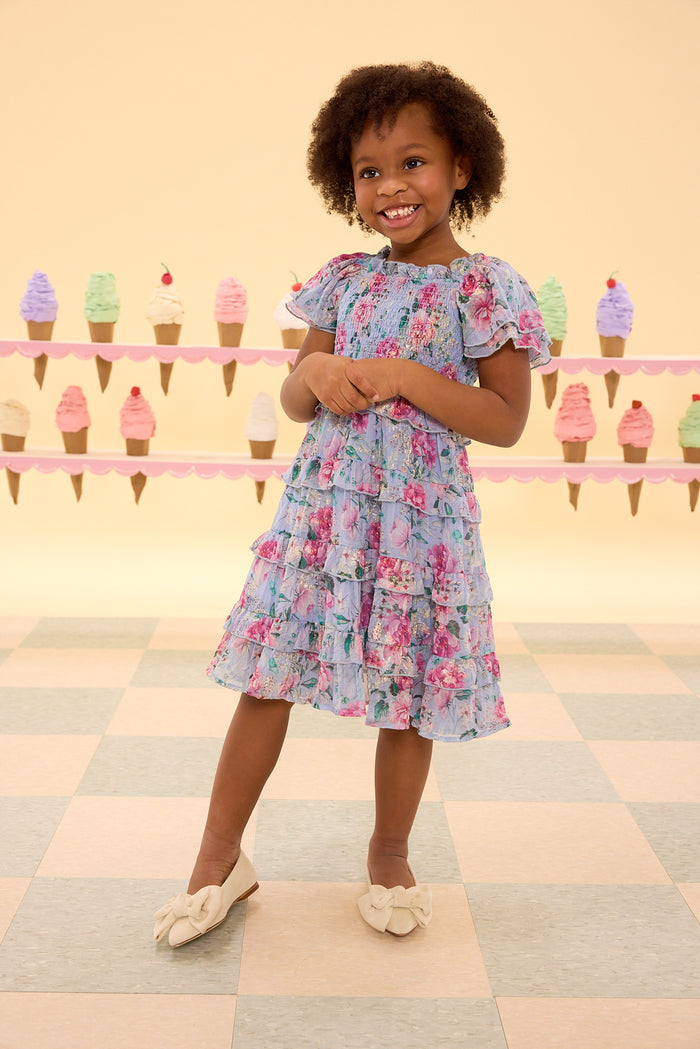 Young girl in a floral dress standing in front of ice cream cone decorations.