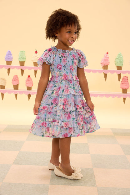 Young girl in a floral dress standing on a checkered floor with ice cream cone decorations in the background.