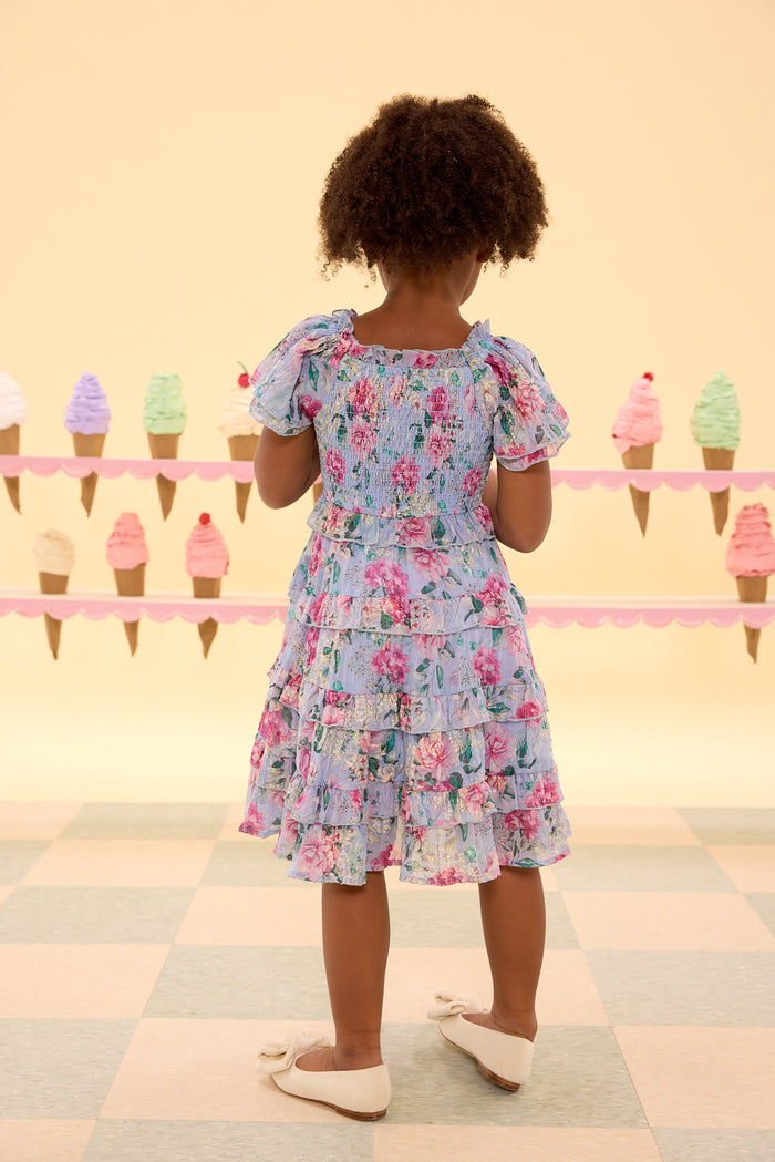 Child wearing a floral dress standing in front of ice cream cone decorations on a checkered floor.
