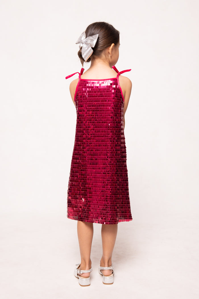 Young girl wearing a red sequin dress with bow straps on a white background