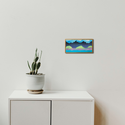 The artwork 'Muffled Saxophone' by Evan Peltzman features an abstract landscape composition with turquoise clouds and coral-colored mountains, framed in wood. The minimalist artwork hangs above a white cabinet with a potted cactus, creating a serene contemporary setting.