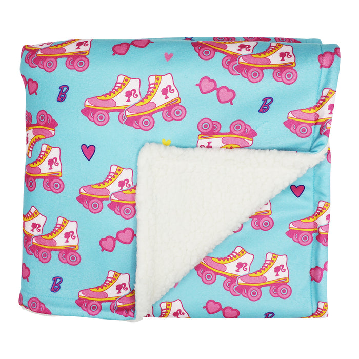 The folded Sassy Woof Pet Blanket - BARBIE™ On a Roll features a blue background with pink/yellow roller skates, hearts, sunglasses, and 'B', plus a white sherpa lining. Part of the Barbie x Sassy Woof collection.