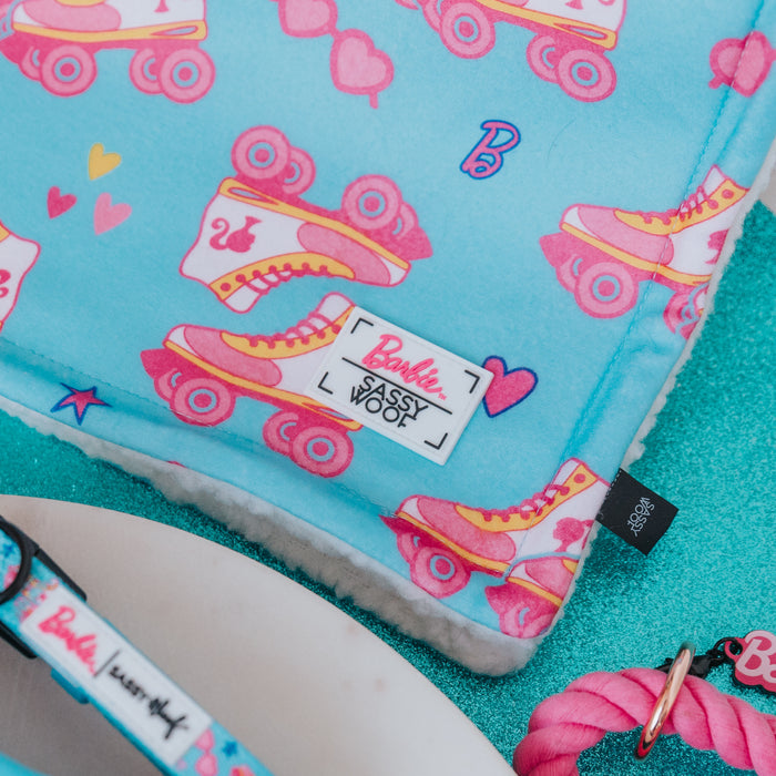 The Sassy Woof Pet Blanket - BARBIE™ On a Roll features blue fabric with pink and yellow roller skate prints, hearts, and the letter B—perfect for your pup and coordinates with other items from the Barbie x Sassy Woof collection.