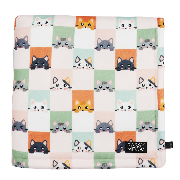 The Pet Blanket - Smitten Kittens by Sassy Woof features a checkered pattern with cartoon cat faces in orange, gray, and white on soft microfiber, plus a black Sassy Woof label at the corner.