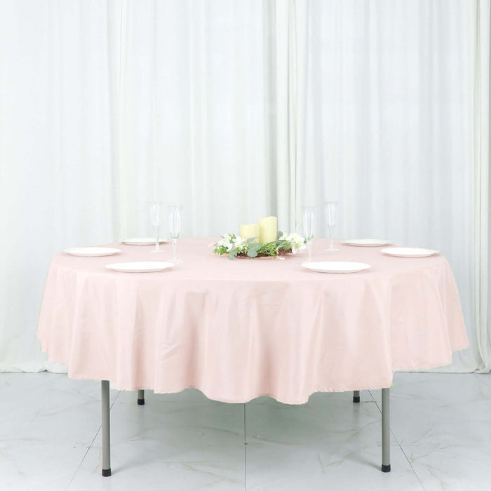 Round pink tablecloth on a dining table with candles and plates arranged neatly.