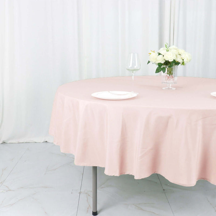 Pink round tablecloth draped over a table with plates and a floral centerpiece.