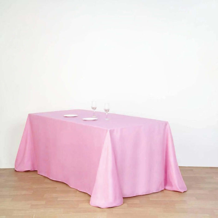 Pink tablecloth draped over a table with plates and glasses on a plain backdrop.