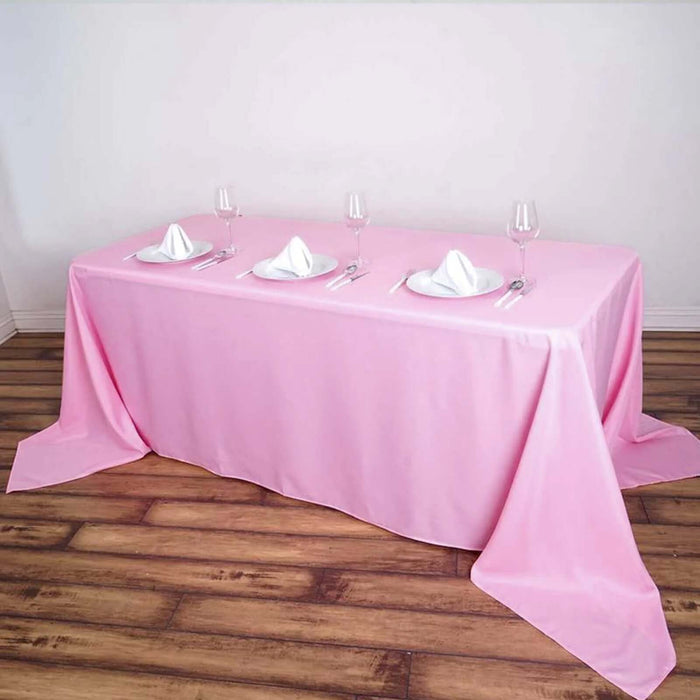 Pink tablecloth set for dining with plates and glasses.