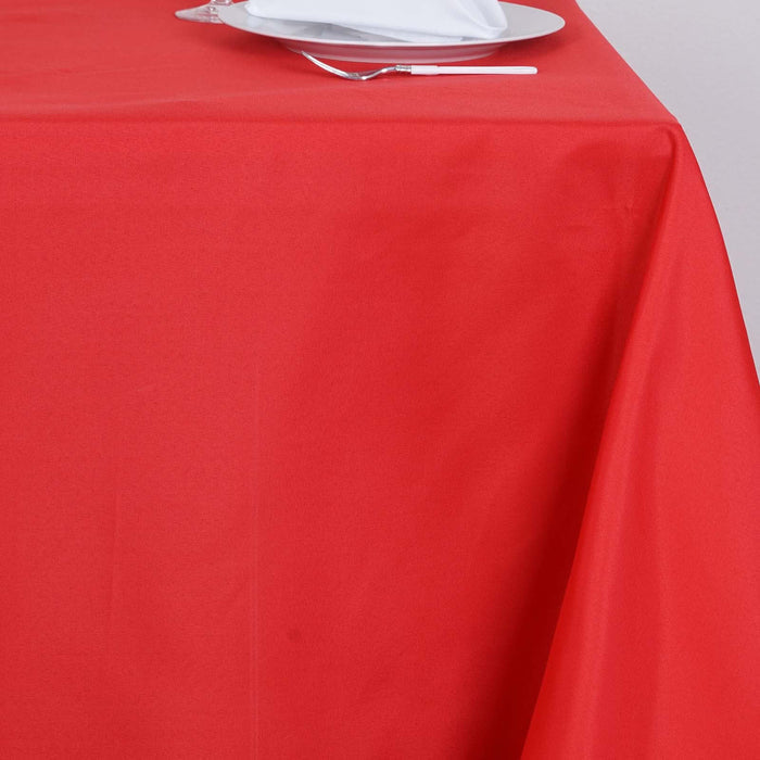 Red tablecloth draped over a table with a white plate and cutlery on top.
